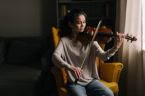 piękna azjatka grająca na skrzypcach, siedząca na miękkim krześle. - practicing music violin women zdjęcia i obrazy z banku zdjęć