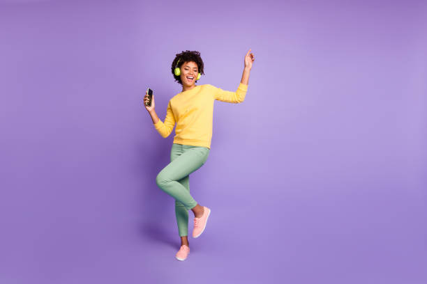 音楽ダンスを聴くヘッドフォンで緑のズボンズボン黄色のセーターの履物を着てトレンディなスタイリッシュなかわいいフリーガールフレンドのフルレングスボディサイズの写真孤立した紫� - music women disco joy ストックフォトと画像