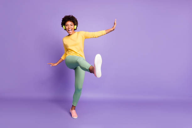 full length body size photo of wavy cheerful excited ecstatic overjoyed shouting girlfriend dancing listening to music pretending to be kicking with leg near empty space isolated over violet color pastel background - chutando imagens e fotografias de stock