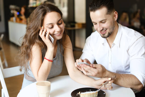 istock Young nice woman talking by smartphone and sitting with man using hotspot at cafe 1181213360