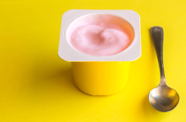 Strawberry pink yogurt in yellow plastic cup isolated on bright yellow background with space for text