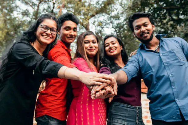 Photo of Close up top view of young people putting their hands together. Indian Friends with stack of hands showing unity and teamwork.