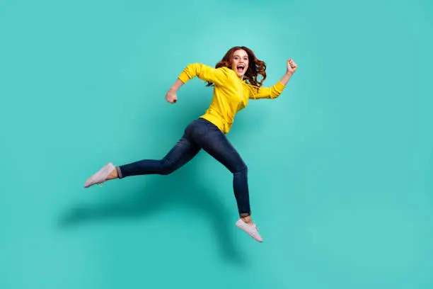 Photo of Full length body size photo of running jumping casual cute nice youngster aspiring for discounted shopping mall in jeans denim isolated turquoise color vivid background
