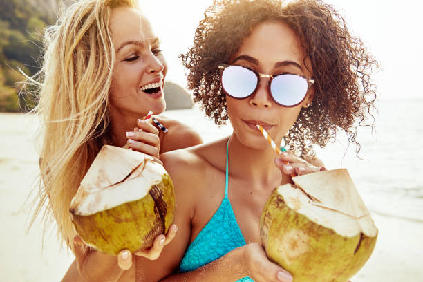 istock Two laughing young women sipping on coconuts at the beach 1181220086