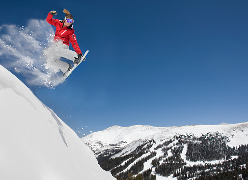 Action Shot of young woman in mid-air making extreme snowboard jump.