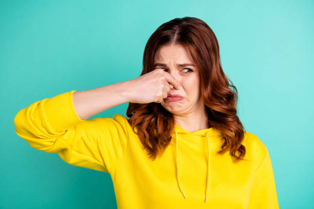 photo of disgusted girl smelling something bad nasty looking shutting her nose isolated over vivid turquoise color background - facial expression unpleasant smell shirt caucasian imagens e fotografias de stock