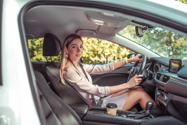 woman wheel of car machine. In summer autumn city. Business lady driving. Background trees. Beautiful girl everyday makeup. Business class sedan. Car sharing in city car rental. stock photo