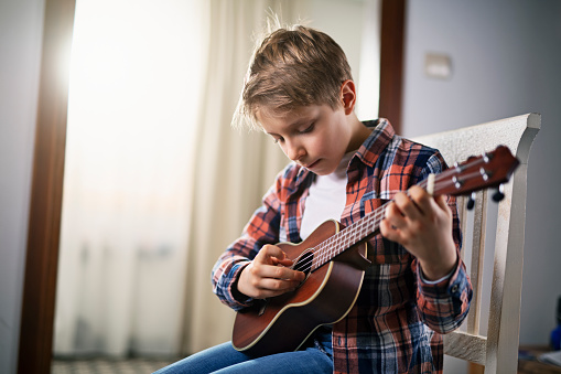 Portrait of a cute 9 year old boy practicing playing guitar at home.\nNikon D850