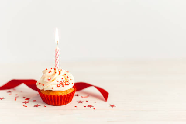 cupcake de cumpleaños con glaseado de crema de mantequilla, cinta roja y vela sobre mesa de madera blanca. - ribbon nobody cupcake celebration fotografías e imágenes de stock