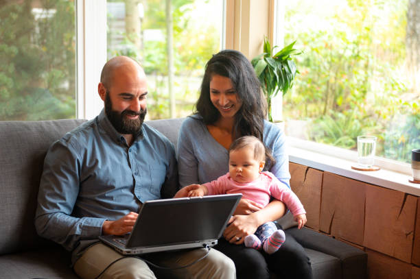 Couple going over home finances with a newborn Couple working from home. Father working from home. Couple doing home finances with a young child. man work from home baby stock pictures, royalty-free photos & images
