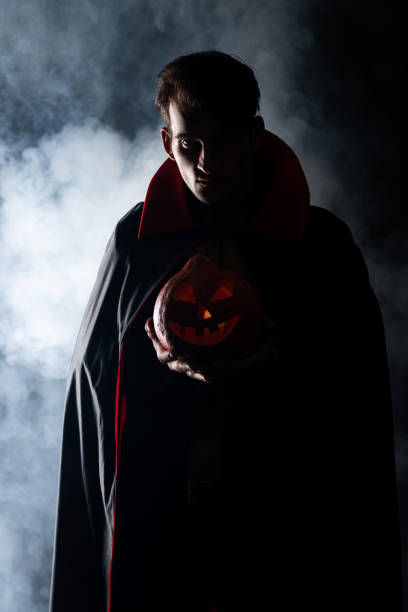 handsome man holding spooky pumpkin on black with smoke
