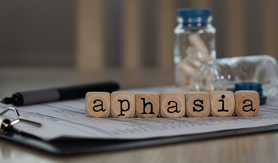 Word APHASIA composed of wooden dices. Pills, documents and a pen in the background. Closeup