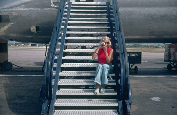 Barbados, Lesser Antilles, 1976. Tourist sitting on a plane gangway filming with an 8mm camera.