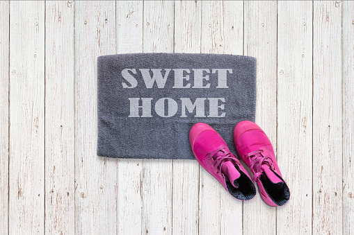 Door mat of home sweet home house entrance with female pink woman shoes flat lying, concept of happy apartment shopping home life