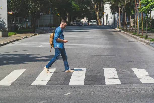 Photo of young man walking at crosswalk on a street.