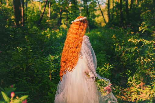 Woman back. Young victorian princess with long hair on nature. Model in veil with bouquet of flowers. Princess in white dress against backdrop of nature. Renaissance imitation. Girl stand back