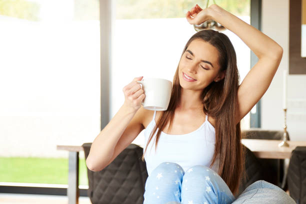 istock Beautiful young woman holding mug in her hand while stretching on sofa 1181247256