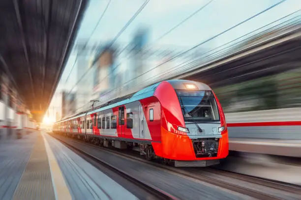 Photo of Electric passenger train drives at high speed among urban landscape.