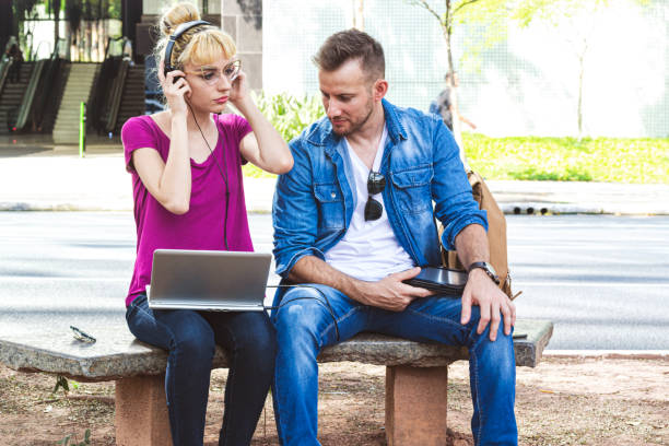 istock Young woman and young man sitting on a bench using a laptop 1181255263