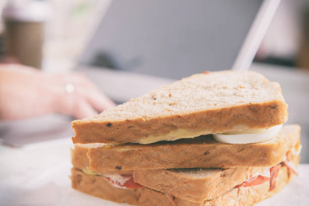 istock Woman eating a breakfast sandwich while working with a laptop 1181257793