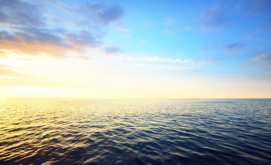 Sunset in a cloudy sky over open Baltic sea with veri distant ship silhouettes.