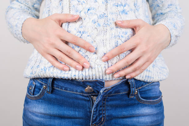 photo de plan rapproché cultivée de fille souffrant des symptômes douloureux dans l'abdomen retenant des mains sur le grand fond gris d'isolement d'isolement de ventre rond - belly button photos et images de collection