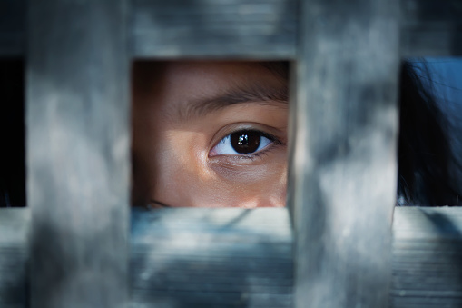The blank stare of a child's eye who is standing behind what appears to be a wooden frame