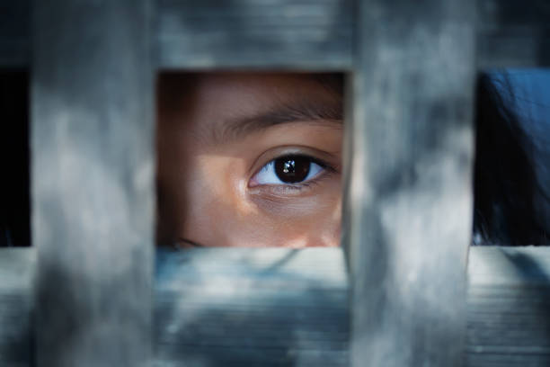 The blank stare of a child's eye who is standing behind what appears to be a wooden frame stock photo