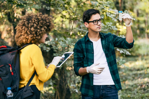 Scientists study water in the forest Men and women scientists are looking at a sample of polluted water in the forest. A scientific ecologist in the forest takes water samples. ecologist stock pictures, royalty-free photos & images