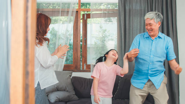 os grandparents e a neta asiáticos escutam a música e a dança junto em casa. o chinês sênior, o grandpa e a avó felizes gastam o tempo da família relaxa com a rapariga no conceito da sala de visitas. - listening child grandfather family - fotografias e filmes do acervo