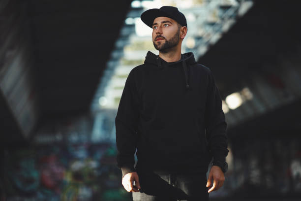 portrait of a young bearded man with a black hat ain black hoodie in the city - camisa de moleton imagens e fotografias de stock