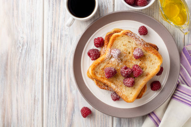 French toasts with powdered sugar and fresh raspberries on wooden table