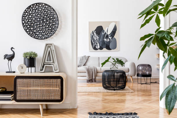 istock Modern scandinavian interior design of open space with stylish wooden commode, gray sofa, rattan coffee table, plant, tropical leaf and elegant personal accessories. Stylish home decor. Template 1181271856
