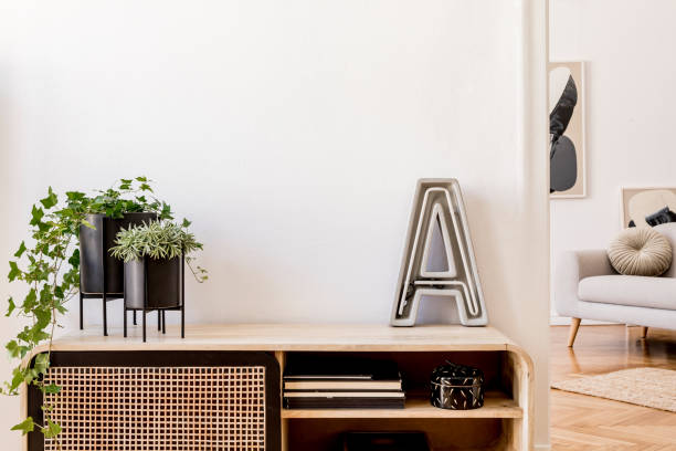 istock Modern scandinavian home interior with design wooden commode, plants in black pots, cement letter, gray sofa, books and personal accessories. Stylish home decor. Template. Copy space. White walls. 1181271926