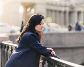 Portrait close-up of beautiful intelligent brunette who walks down street of St. Petersburg in city center. Charming thoughtful woman with long dark hair wanders alone, immersed in thoughts