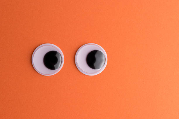 Googly eyes on orange background. Minimal holiday concept.