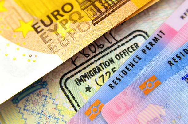 UK BRP Tier 2 visa card and 50 Euros are placed on top immigration stamp in passport. stock photo