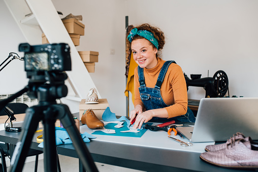 Young woman filming the video blog about making leather shoes in her workshop.