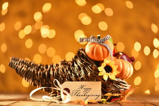 Thanksgiving still life cornucopia and pumpkins with a greeting card and illuminated background on a rustic wooden table