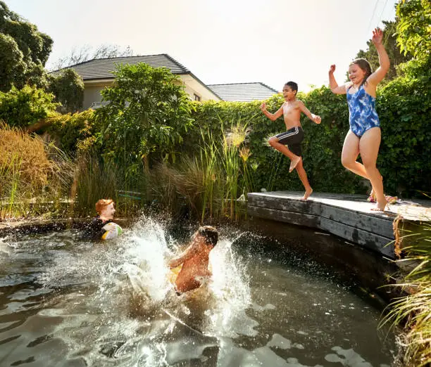 Shot of children jumping into an outdoors pool on a summer day