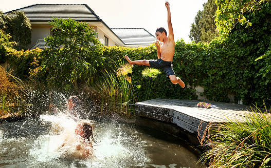 Shot of little children jumping into an outdoors pool on a summer day