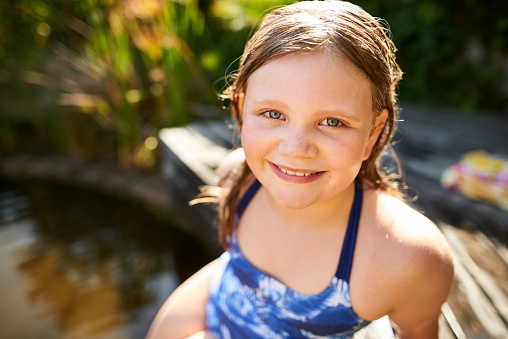 Close up shot of beautiful little girl in swimwear sitting by a pool outdoors