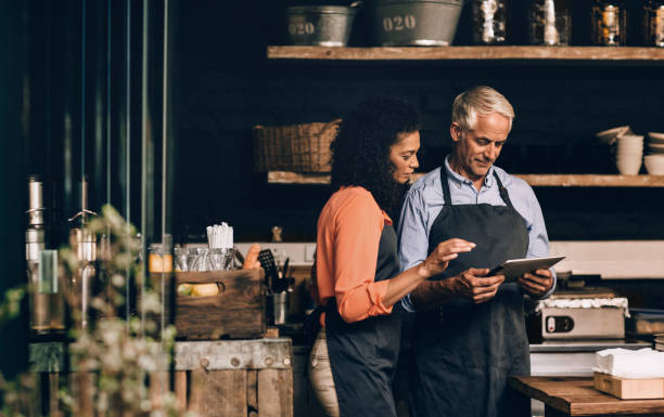 istock Mature couple smiling while using a tablet in their cafe 1181305992