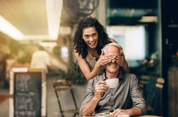 istock Laughing woman surprising her husband sitting at a cafe 1181310020