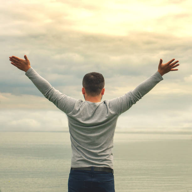 istock A young man is standing on the shore. The view from the back. Yoga classes. Hands raised up. Freedom and achievement. 1181316676