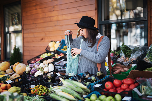 Young woman buying fruit and vegetables at outside market, she putting vegetable in carrying bag.