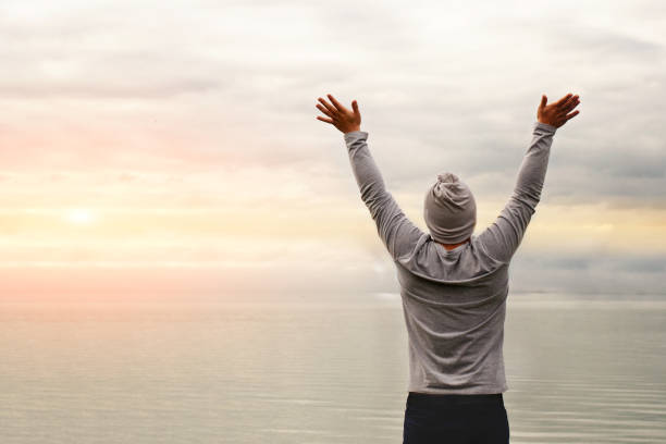 istock A young man is standing on the shore. The view from the back. Yoga classes. Hands raised up. Freedom and achievement. 1181317410