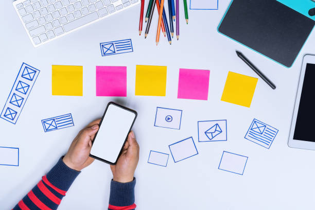 istock Ux designer hands holding white screen smartphone mockup on white office desk. User Experience Design Process concept. 1181340000