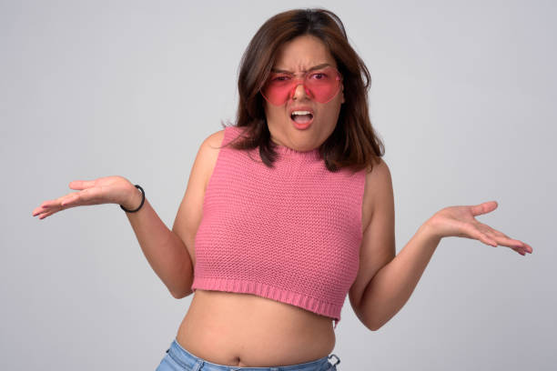 giovane donna asiatica confusa con occhiali a forma di cuore che alzano le spalle - bassiera foto e immagini stock