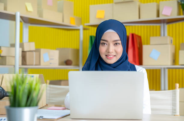 Young asian muslim woman in hijab dress is working at home typing on through laptop.. Small business owner and online marketing and SME concept. stock photo
